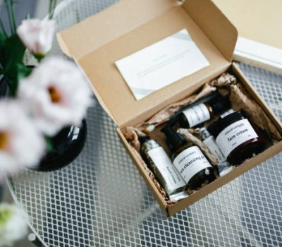 Shot from above of an open gift box on the coffee table. There are natural cosmetic products inside and paper note.