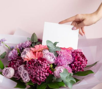 Womens hand holding blank paper card over beautiful bouquet of colorful flowers. Love, Birthday, Valentines day concept