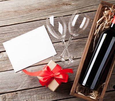 Valentines day greeting card. Red wine and gift box on wooden table. Top view with copy space